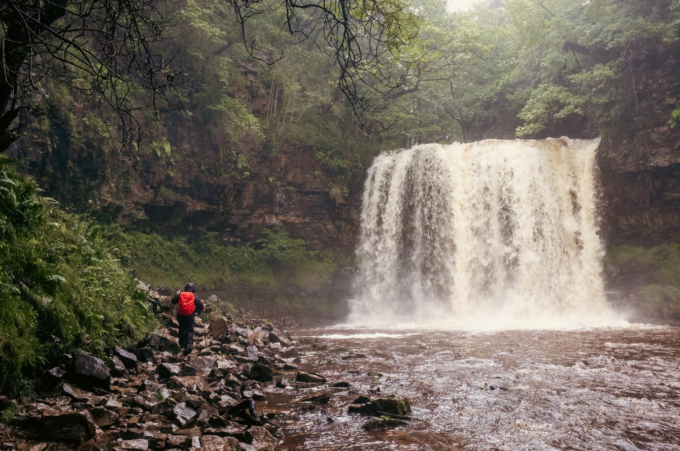 waterfall in forest with walker wearing red rucksack