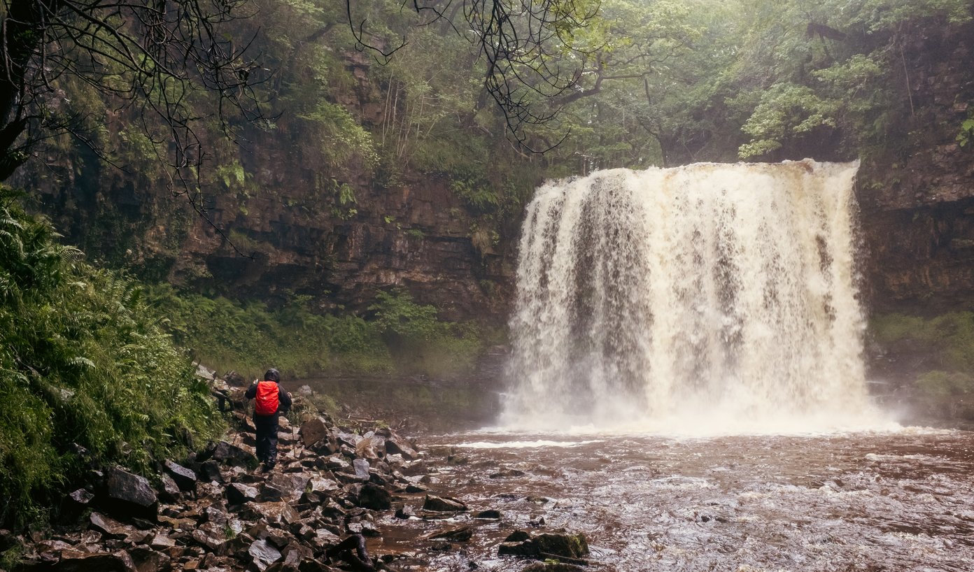 waterfall in forest with walker wearing red rucksack