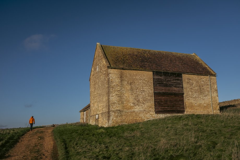 man in orange jacket walking past barn