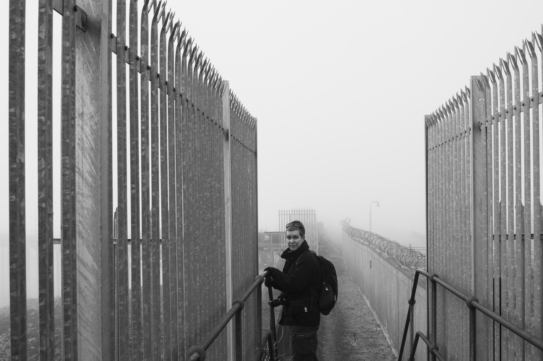 woman on footpath between metal fencing