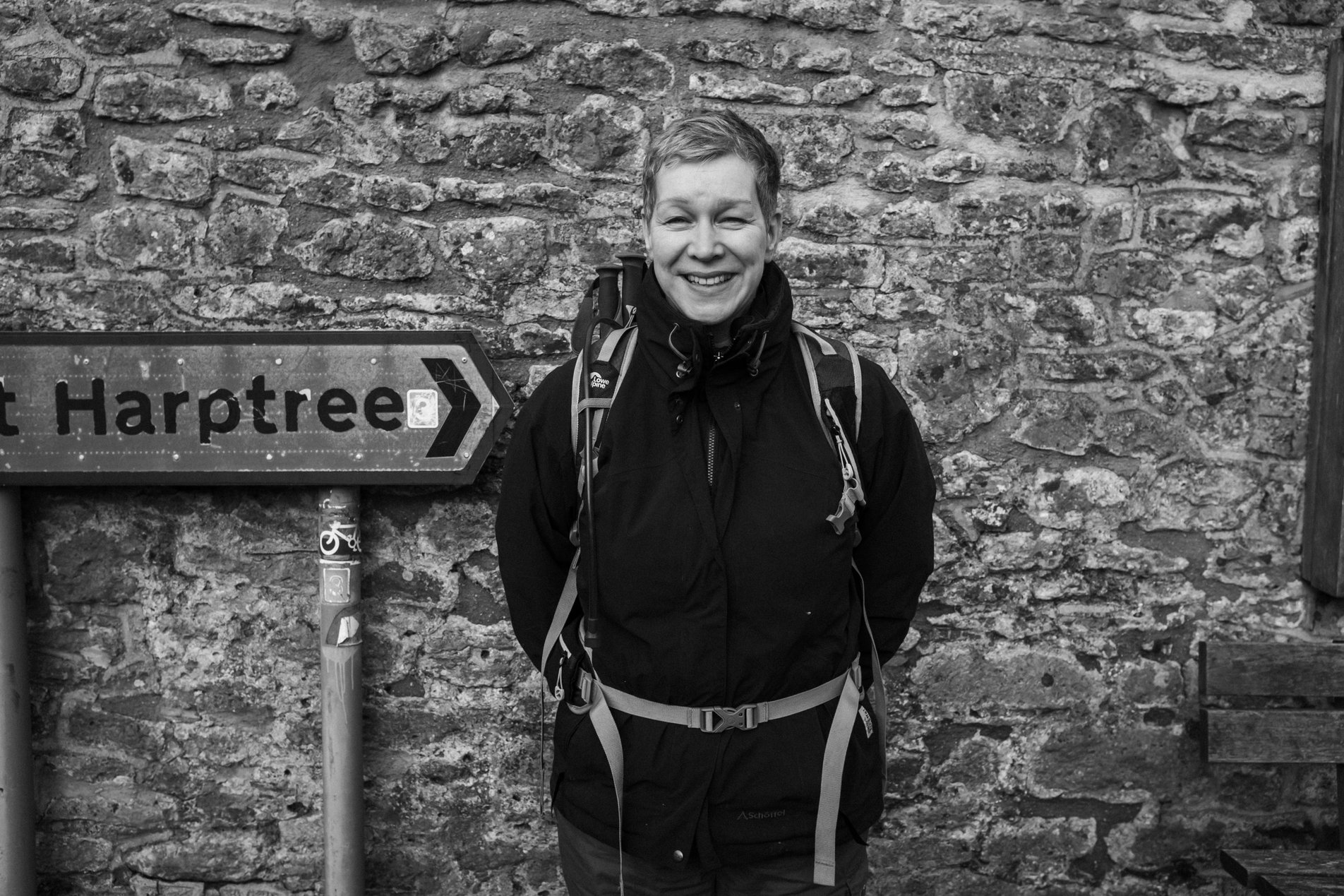 woman grinning standing next to stone wall and road sign