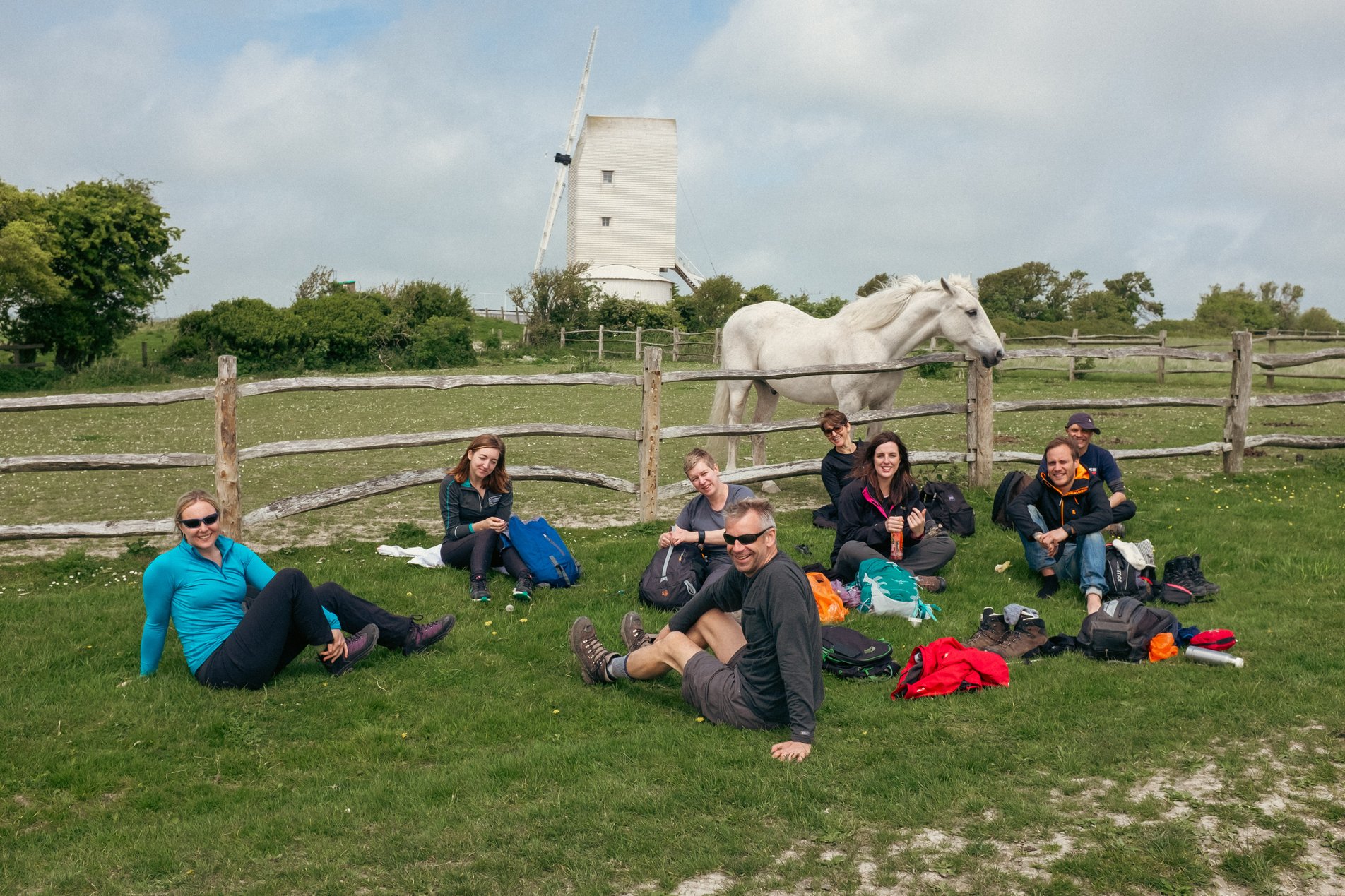 group of hikers having lunch next to field with horse and windmill