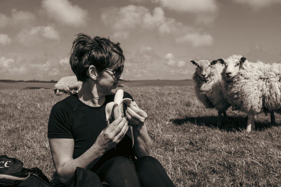 hiker eating banana whilst looking at approching sheep