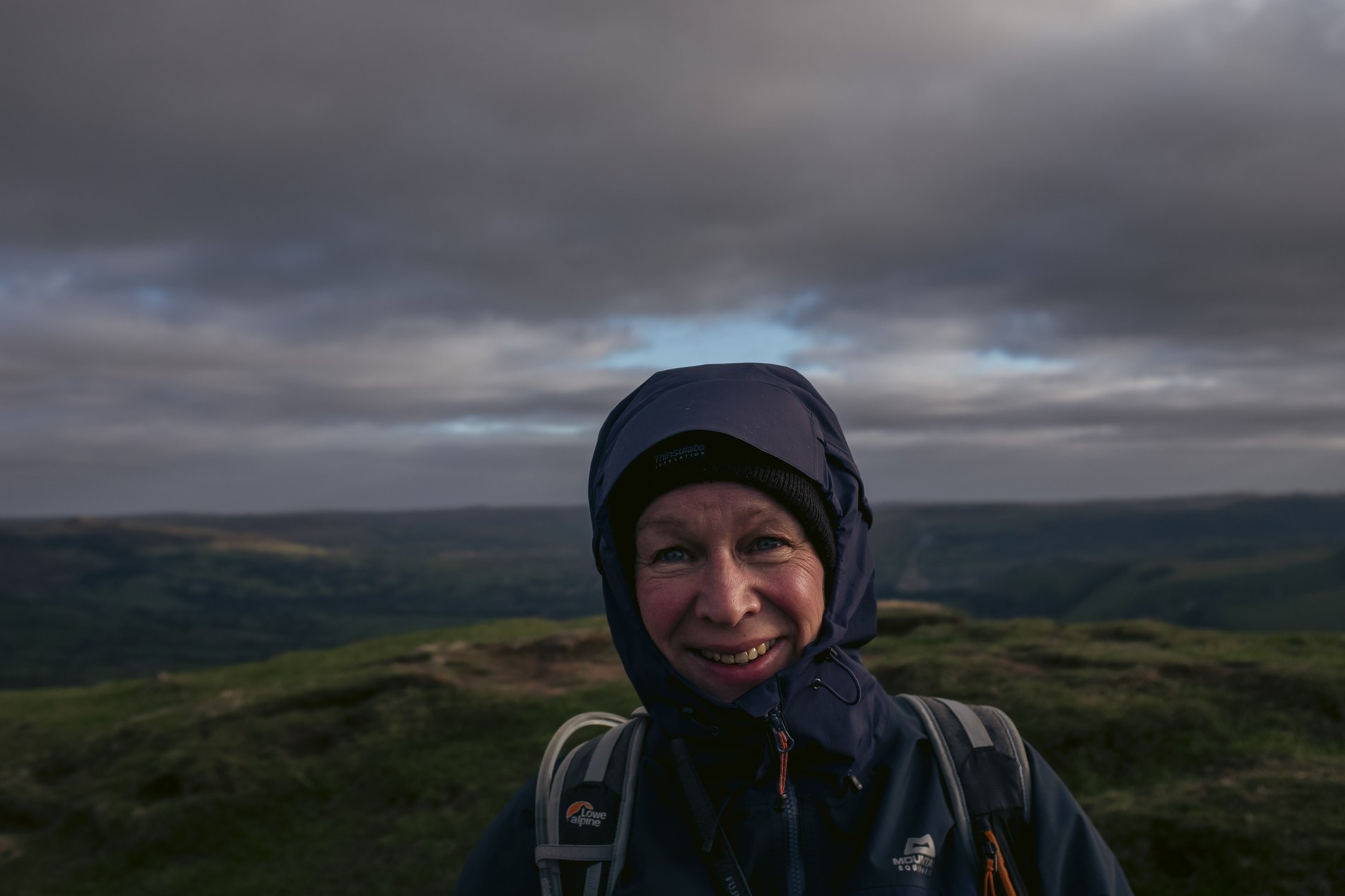 hiker smiling in hooded jacket on hillside