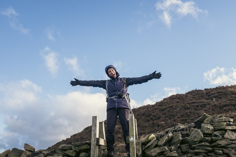 hiker with hands raised on ladder over dry stone wall