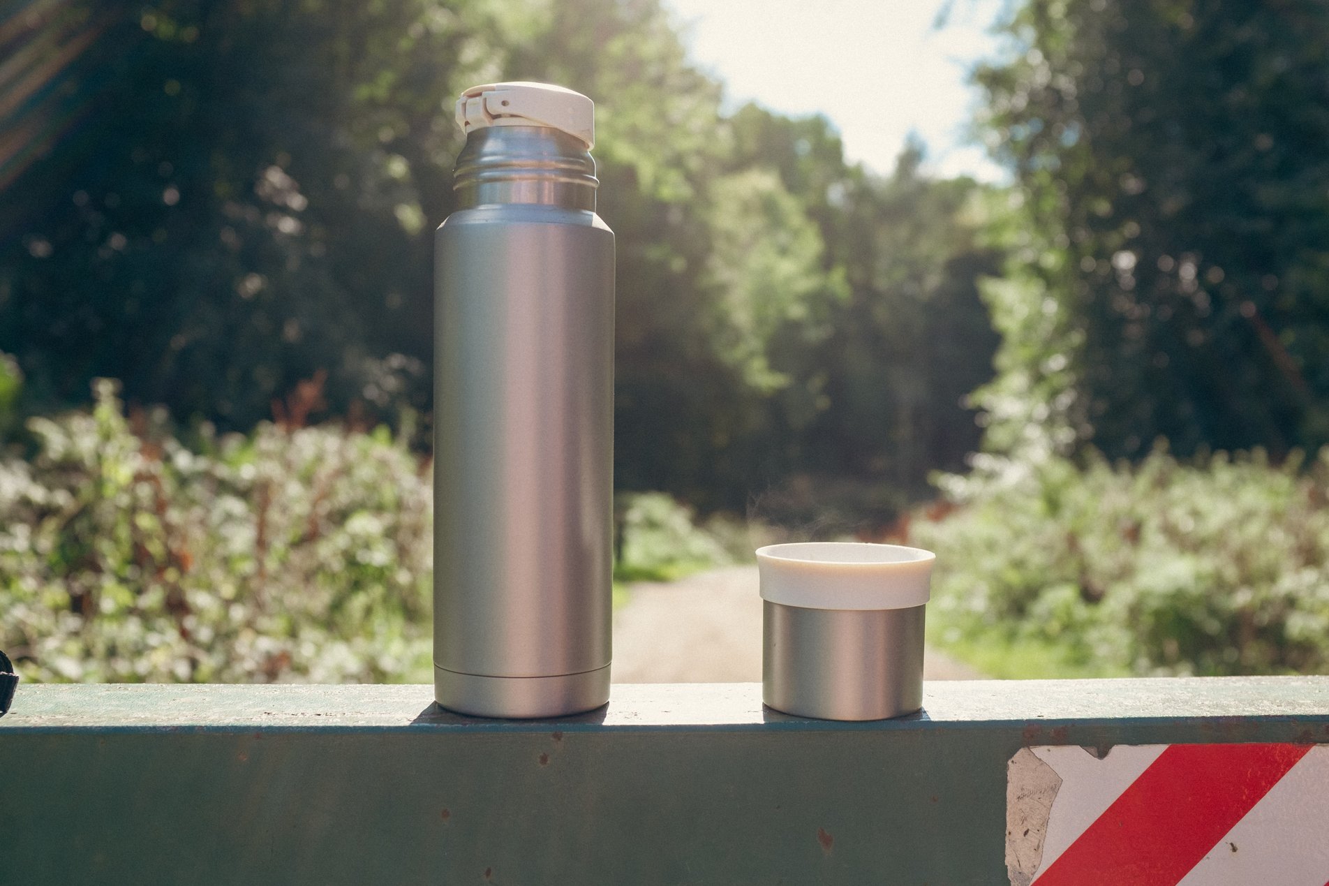 sliver flask of coffee standing on forest gate